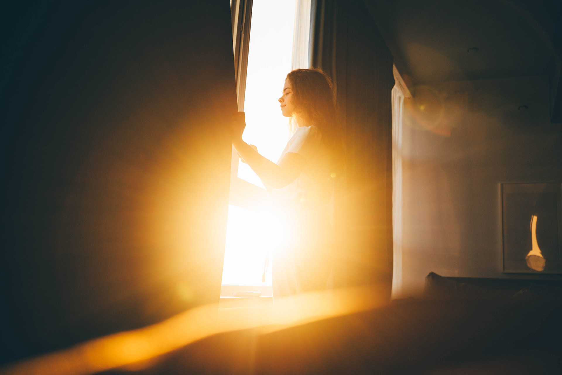 Woman standing near big window at sunrise.